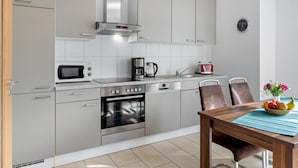 A modern kitchen with stainless steel appliances, a built-in oven, and a dining area with a wooden table and chairs. - Group house with sauna on the Baltic Sea (Boiensdorf)