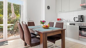 A modern kitchen with stainless steel appliances, a dining area with a wooden table and chairs, and a sliding glass door leading to an outdoor patio. - Group house with sauna on the Baltic Sea (Boiensdorf)