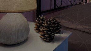 A bedside table with a lamp, a pine cone, and a bed with a patterned headboard.