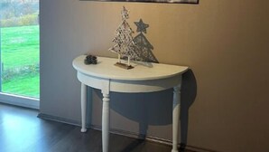 A room with a large window, a white console table with a Christmas tree and star decoration, and a painting of a bull's head on the wall.