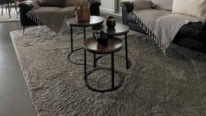 A modern living room with a sofa, two coffee tables, a rug, and a large mirror on the wall.