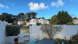 Une terrasse extérieure avec une table et des chaises, un chien, et une vue sur des maisons en arrière-plan.