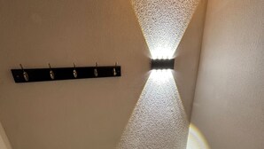 Un coin de pièce avec un plafond en bois, un luminaire fixé au mur qui projette une ombre, et une étagère noire dotée de crochets.