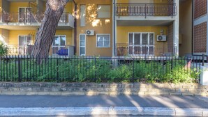 Un edificio giallo a più piani con balconi, condizionatori d'aria e un albero sullo sfondo.