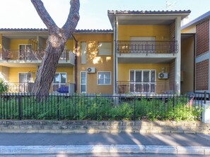 A multi-story yellow building with balconies, air conditioning units, and a tree in the foreground.