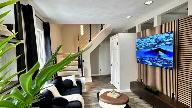 Un salon moderne avec un canapé, un pouf et un téléviseur à écran plat fixé sur un mur recouvert de panneaux en bois.