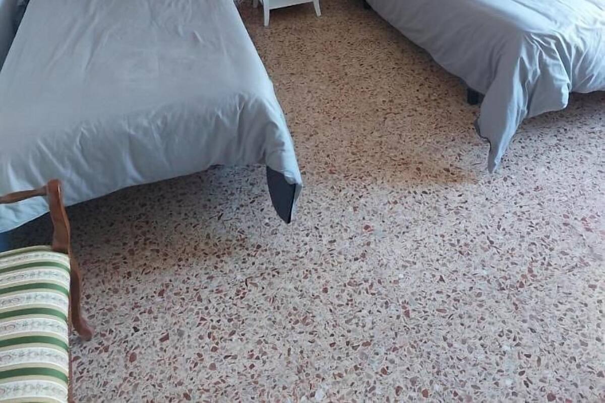 Une chambre avec deux lits, une petite table de chevet blanche avec une lampe et un radiateur.