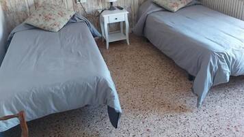 Een kamer met twee bedden, een klein wit nachtkastje met een lamp en een radiator.