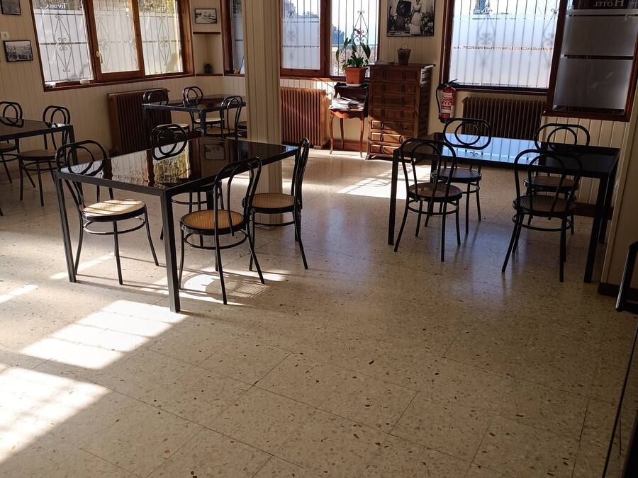 Un vaste espace de restauration dans l’hôtel, avec de nombreuses tables et chaises, de grandes fenêtres équipées de stores et un extincteur fixé au mur.