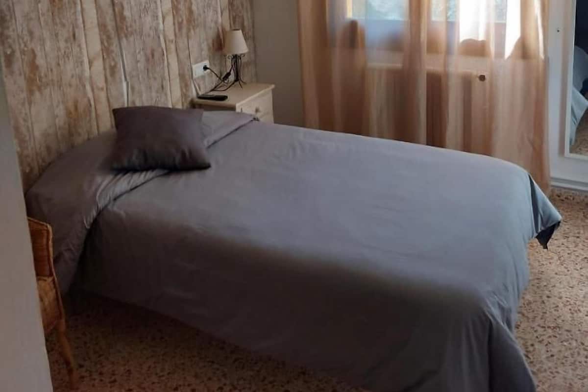 Une chambre à coucher avec un lit, une table de chevet, une lampe, un mur en bois et une fenêtre avec des rideaux.