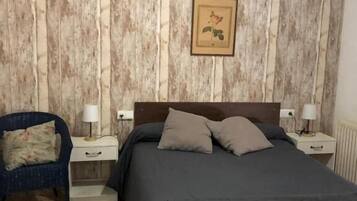 Ein Schlafzimmer mit Holzpaneelen, einem Bett mit grauer Bettwäsche, zwei Nachttischen mit Lampen, einem Sessel und einem gerahmten Bild an der Wand.