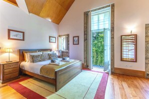 Une chambre à coucher avec un lit, des tables de chevet, une fenêtre et une vue sur la verdure.