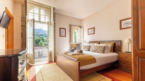 Ein Schlafzimmer mit Bett, Nachttischen, einem Schminktisch, einem Fernseher und Blick auf Grünflächen.