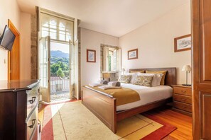 Ein Schlafzimmer mit Bett, Nachttischen, einem Schminktisch, einem Fernseher und Blick auf Grünflächen.