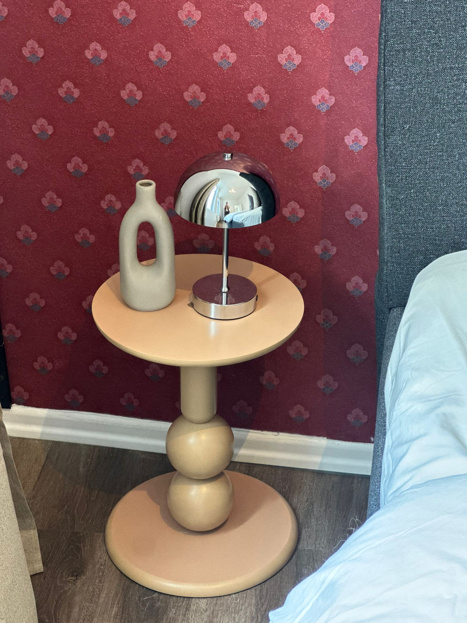 A round table with a vase and a mirror, set against a red floral wallpaper.