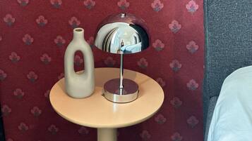 A round table with a vase and a mirror, set against a red floral wallpaper.