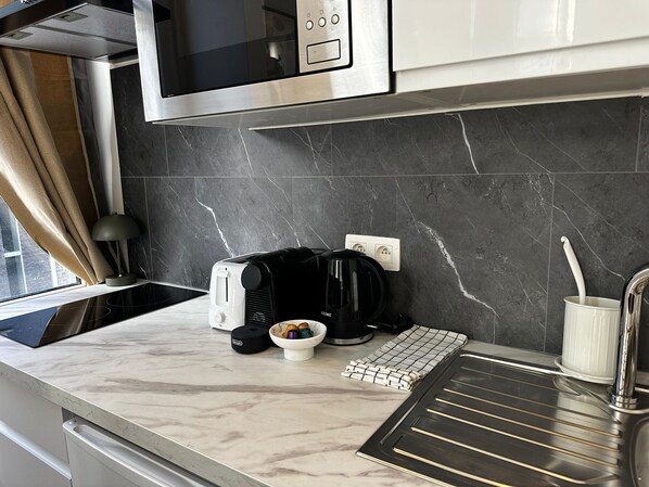 Une cuisine moderne équipée d’un four à micro-ondes, d’un grille-pain, d’une machine à café et d’un saladier rempli de fruits posé sur le plan de travail.