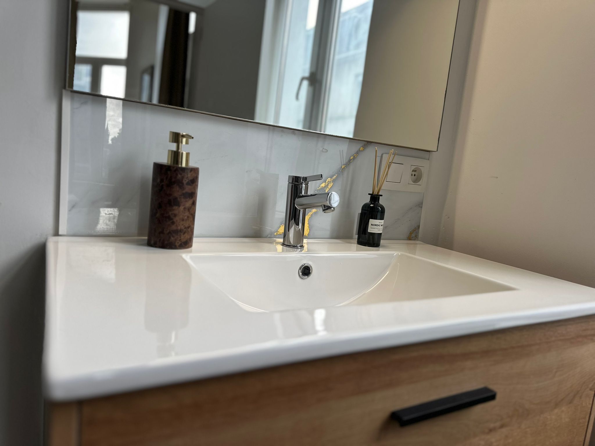 Un baño con un lavamanos blanco, un espejo y un mueble de madera.