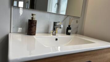 Un baño con un lavamanos blanco, un espejo y un mueble de madera.