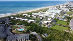 Luftaufnahme eines Küstenresorts mit mehreren Gebäuden, einem Strand und einem Schwimmbad.