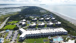Ein Luftbild eines Küstenhotels mit mehreren Gebäuden, einem Schwimmbad und einem Strand.