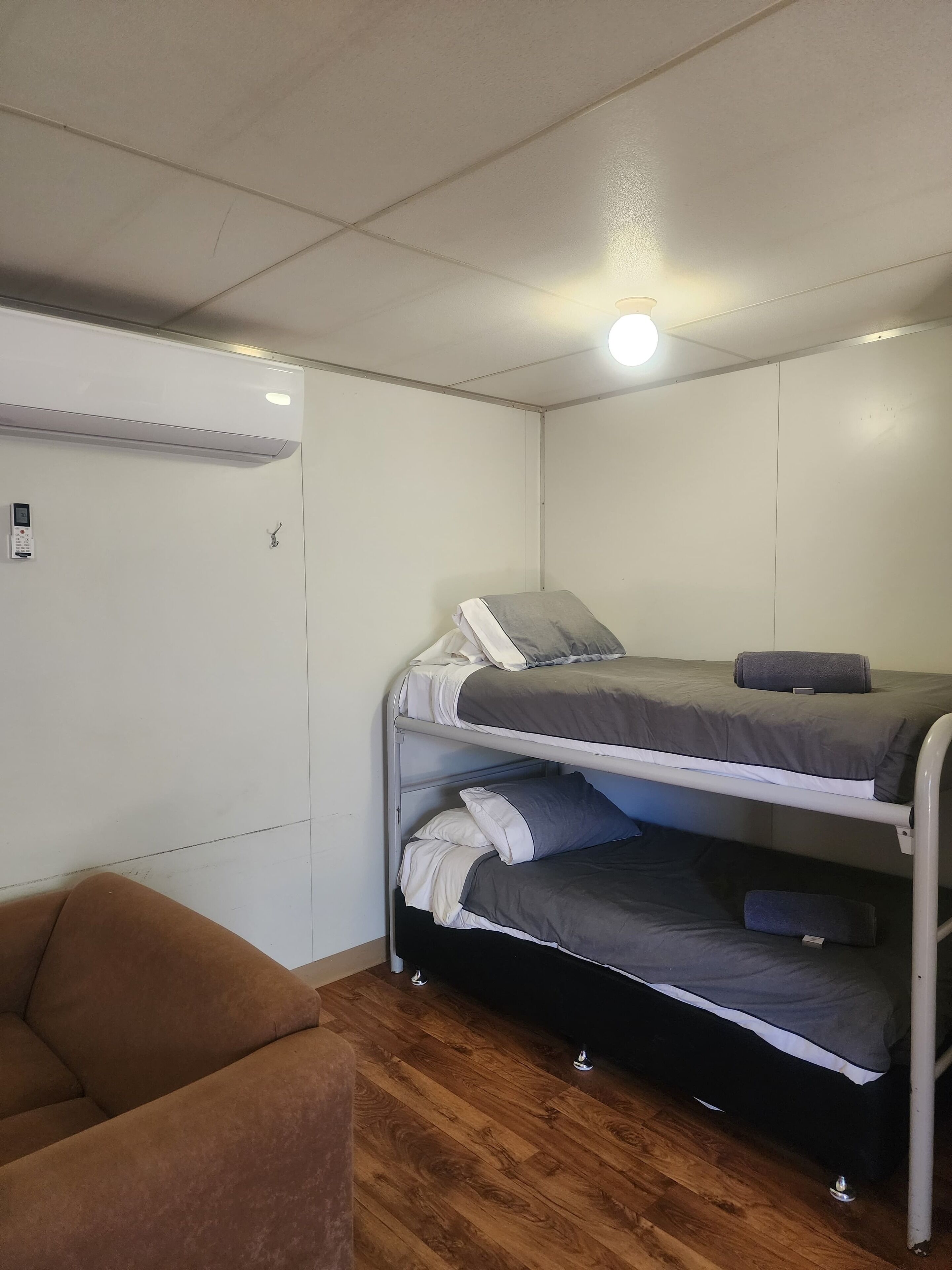 Een stapelbed met grijze beddengoed, een bruine stoel en een plafondlamp.