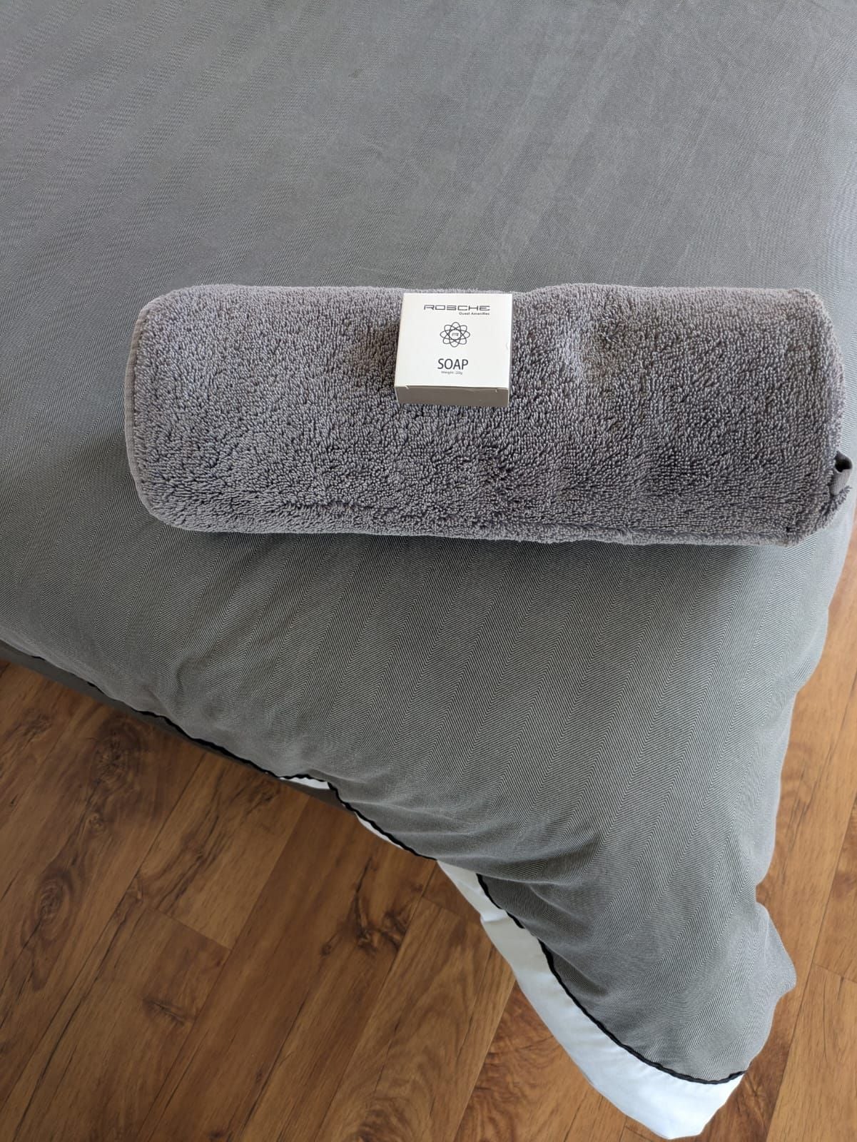 A rolled-up grey blanket with a label on a grey pillow on a wooden floor.