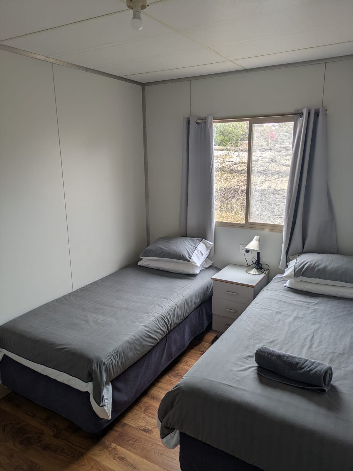 Une chambre avec deux lits simples, une table de chevet avec une lampe et une fenêtre avec des rideaux.