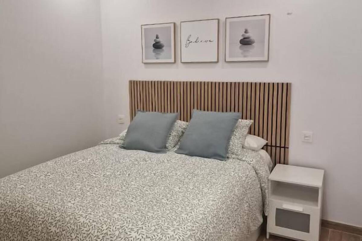Une chambre à coucher avec un lit, deux oreillers, une table de chevet et trois tableaux encadrés accrochés au mur.