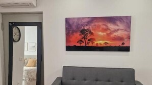 Un soggiorno con un divano grigio, un quadro raffigurante un tramonto e una porta che dà su un'altra stanza.