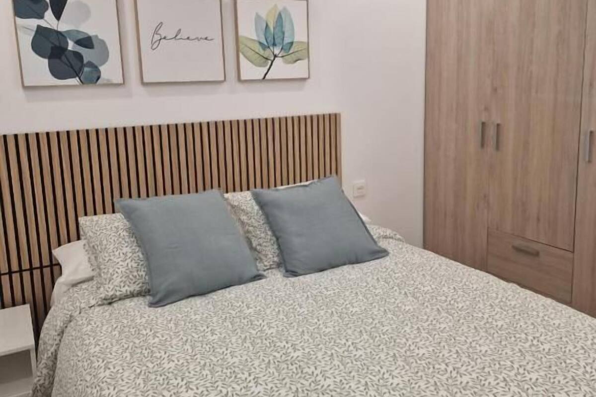 Une chambre à coucher avec un lit, une armoire en bois et trois œuvres d’art encadrées accrochées au mur.
