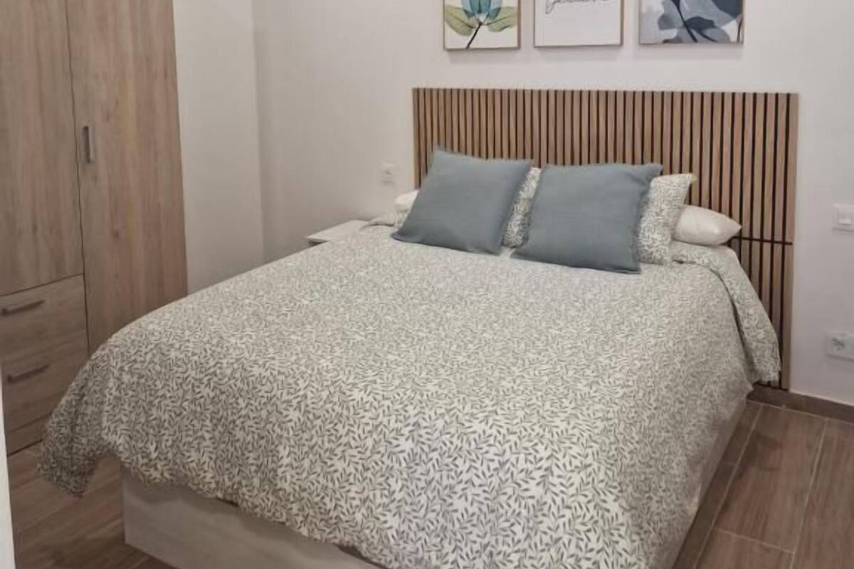 Une chambre à coucher avec un lit, une armoire en bois et trois œuvres d’art encadrées accrochées au mur.