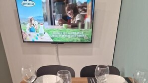 Un tavolo da pranzo per quattro persone, con un televisore appeso alla parete che mostra un programma.