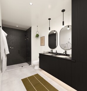 A modern bathroom with dark cabinetry, a white toilet, two sinks, and a shower area.