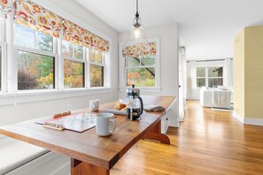 A bright kitchen with a wooden table, a coffee maker, and a view of autumn trees through large windows. - Spacious Living, Covered Porch & Forest Setting | Beaver Creek by AvantStay (Stockbridge)