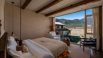 Un dormitorio amplio con una cama grande, vistas a las montañas y un balcón con mobiliario exterior.
