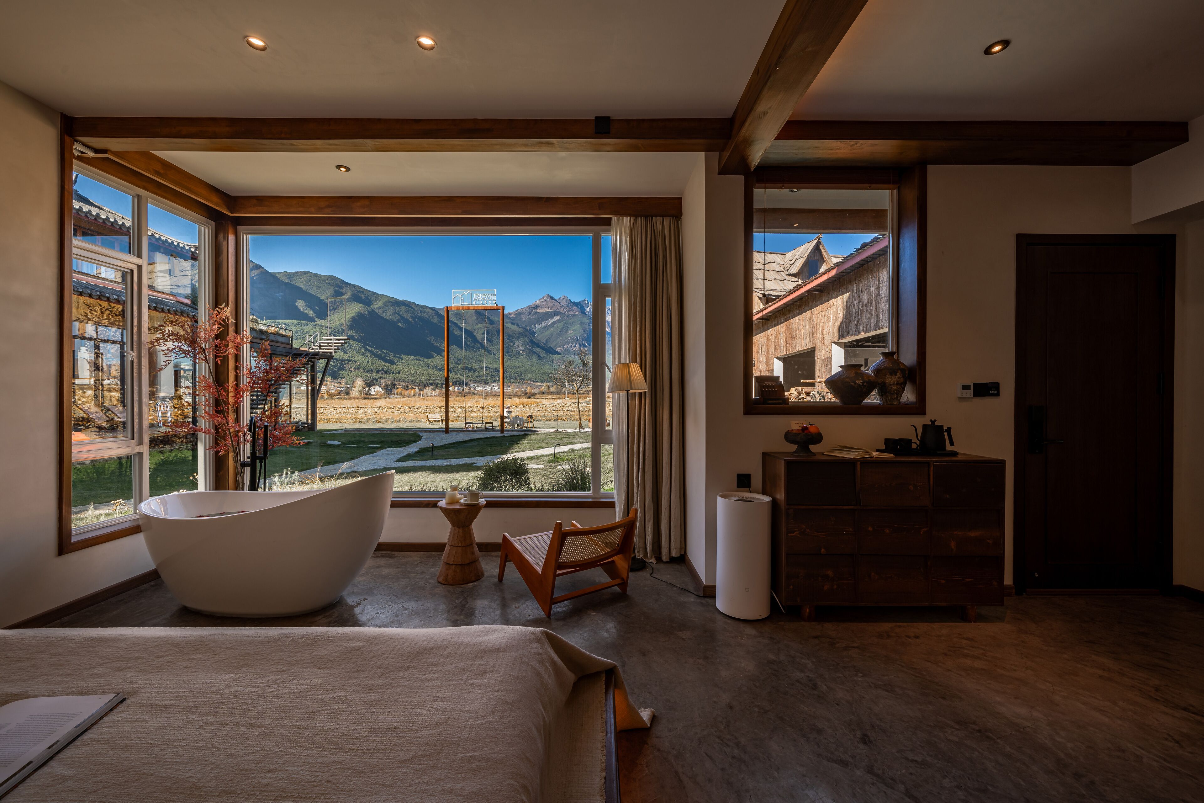 A modern bedroom with a large window, a bathtub, a wooden chair, and a dresser.