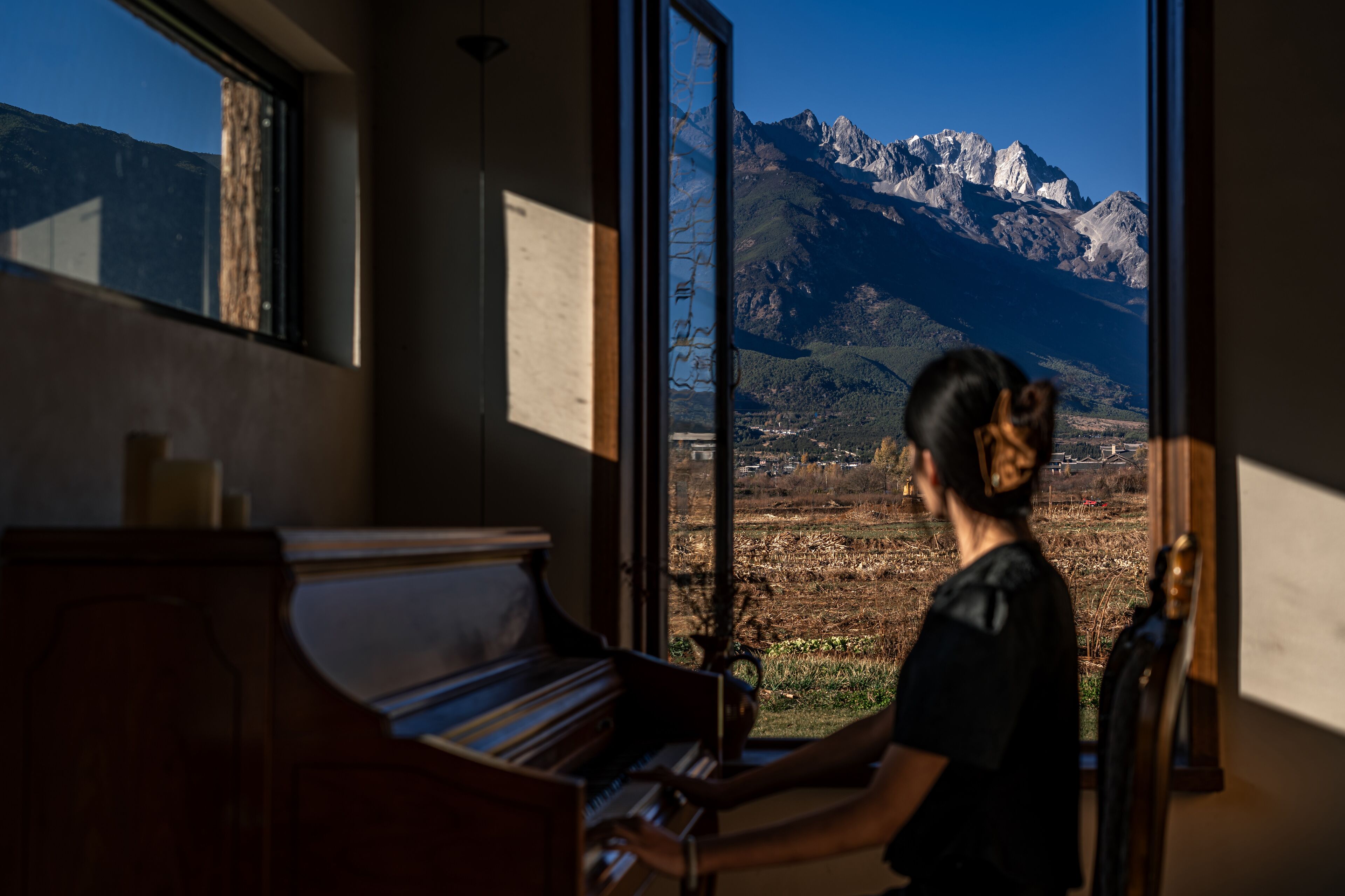 A piano in a room with a large window overlooking a mountainous landscape.