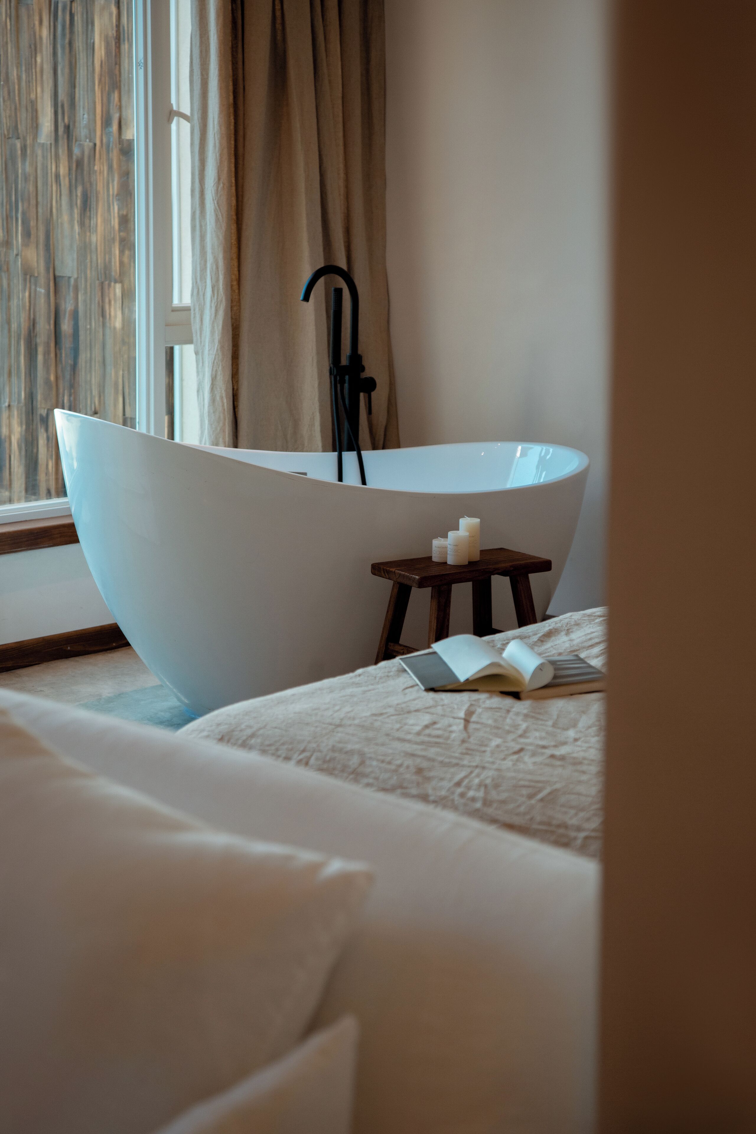 A modern bathroom with a freestanding bathtub, a small wooden stool, and candles.