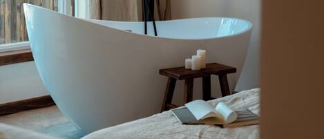 A modern bathroom with a freestanding bathtub, a small wooden stool, and candles.
