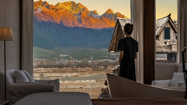 Habitación de hotel con un amplio ventanal que ofrece vistas a montañas y un pueblo en la falda.
