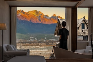Ein Hotelzimmer mit großem Fenster und Blick auf Berge sowie ein Dorf darunter.
