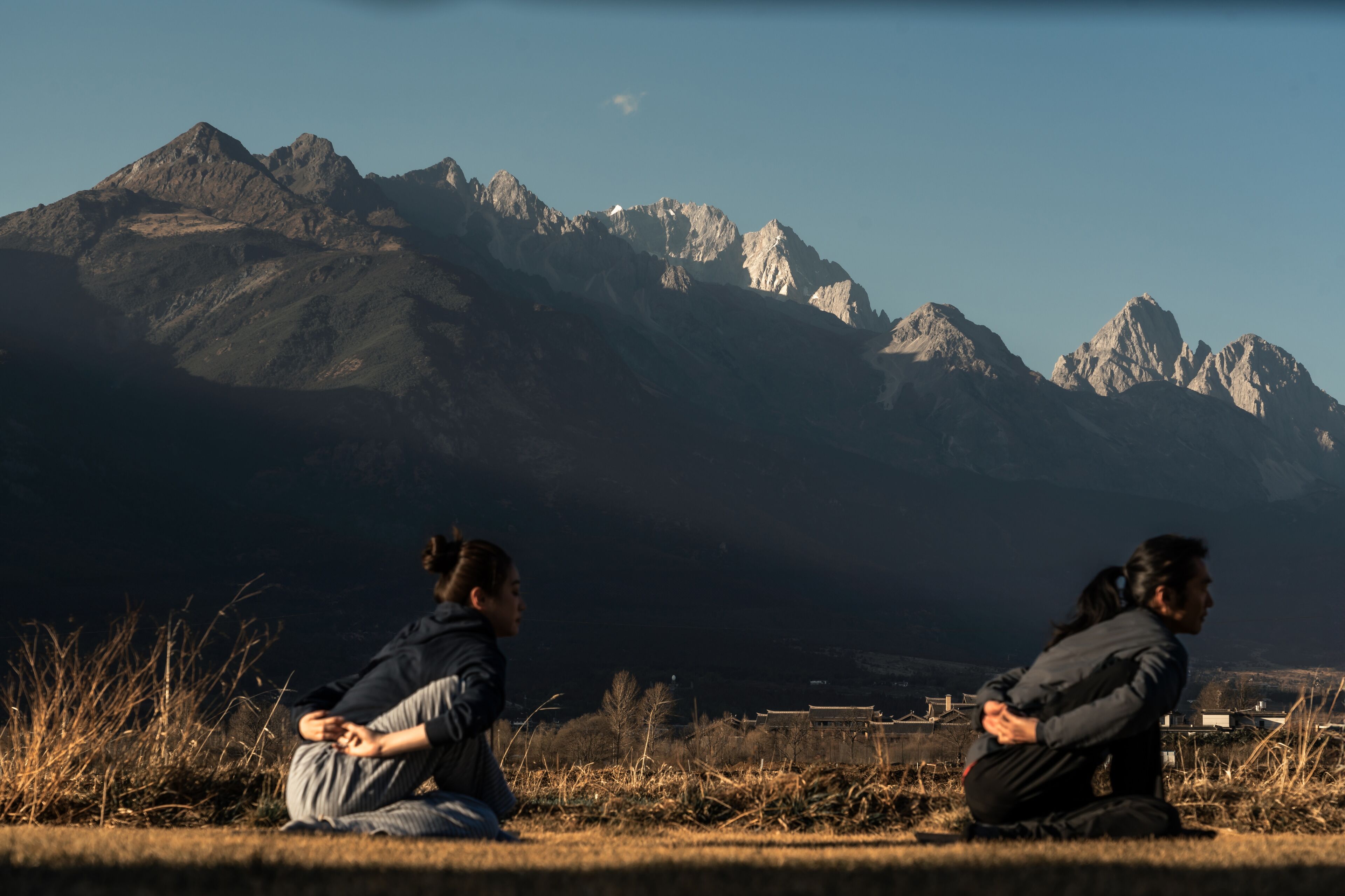 Two individuals sitting on the ground with a mountainous landscape in the background.