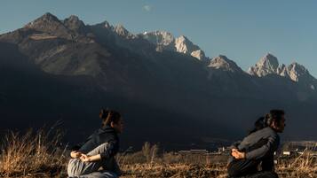Two individuals sitting on the ground with a mountainous landscape in the background.