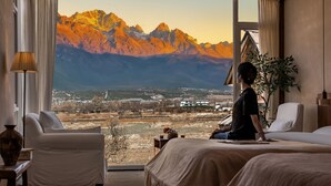 Habitación con amplia ventana y vistas a la montaña, cama, silla y lámpara.