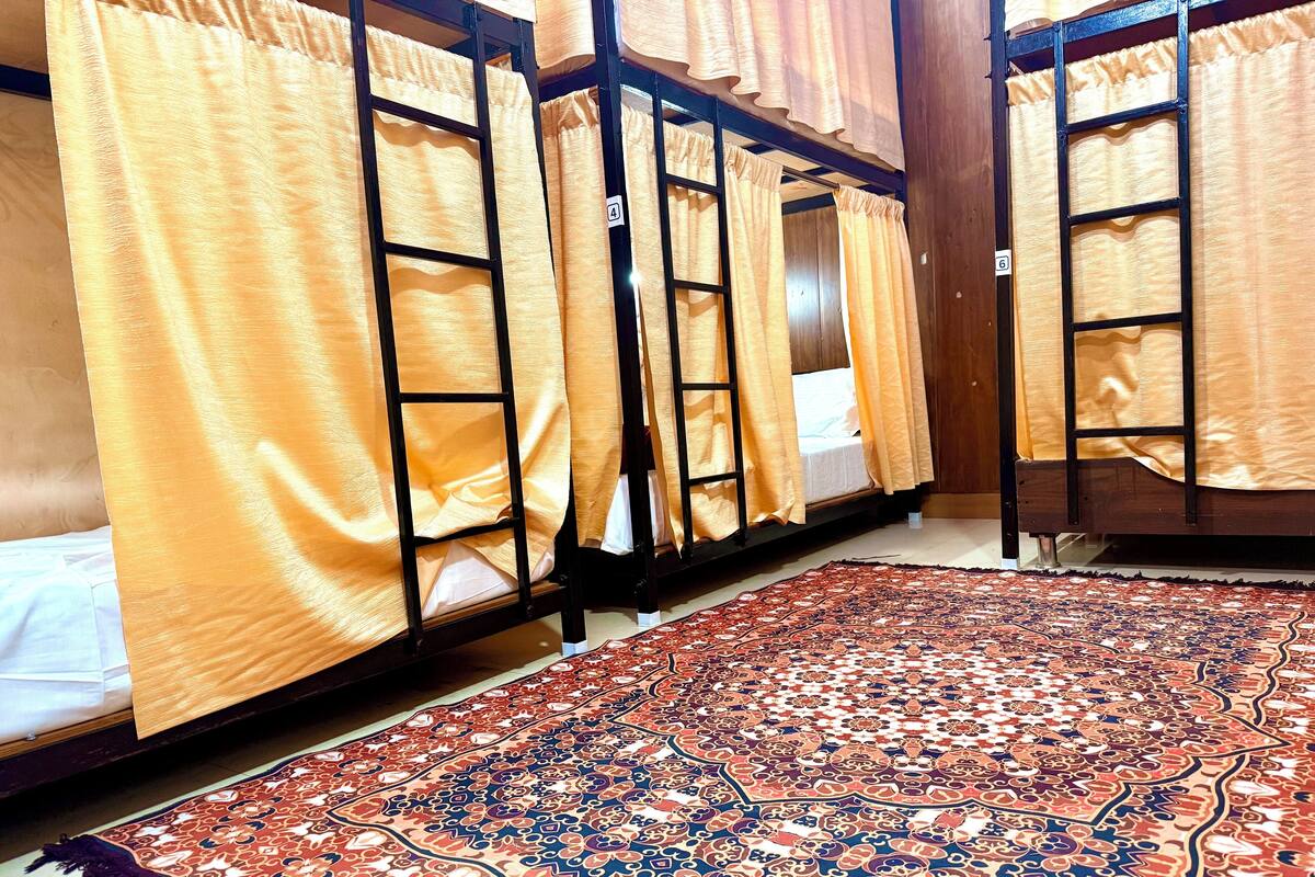 A room with bunk beds, each with a curtain. There is a patterned rug on the floor.