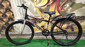 Una bicicleta con estructura negra y detalles rojos, sobre una superficie verde con un mural de fondo.
