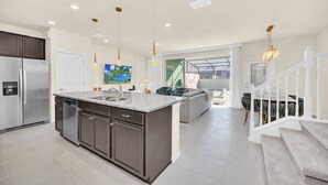 Een moderne keuken met een ruim eiland, roestvrijstalen apparatuur en hanglampen.