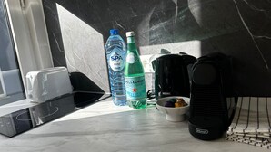 Eine Küchenarbeitsplatte mit einem Toaster, zwei Wasserflaschen, einem Wasserkocher, einer Kaffeemaschine und einer Schüssel mit bunten Gegenständen.
