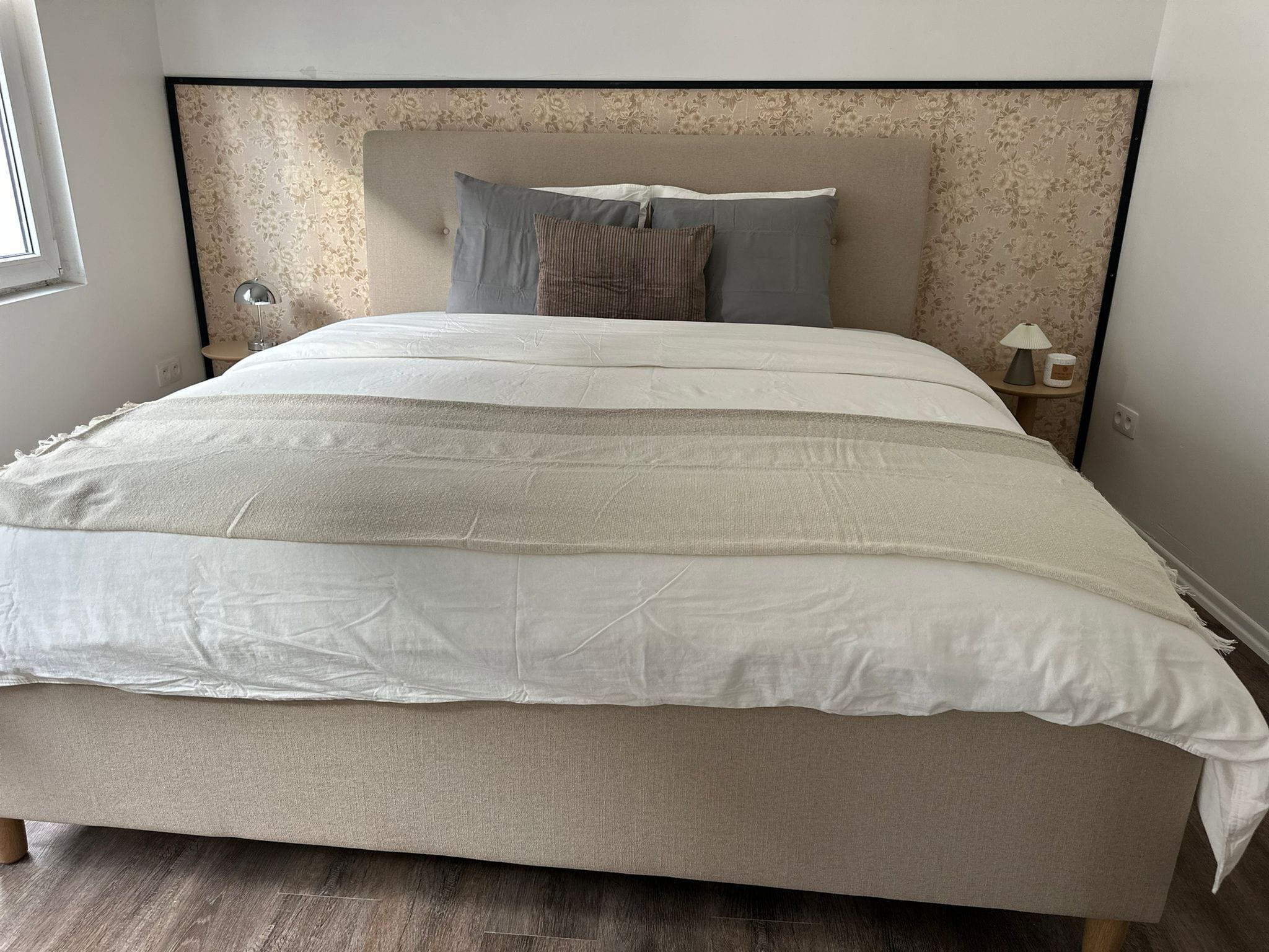 Una cama con cabecera, varios almohadones y una mesita de noche con lámpara.
